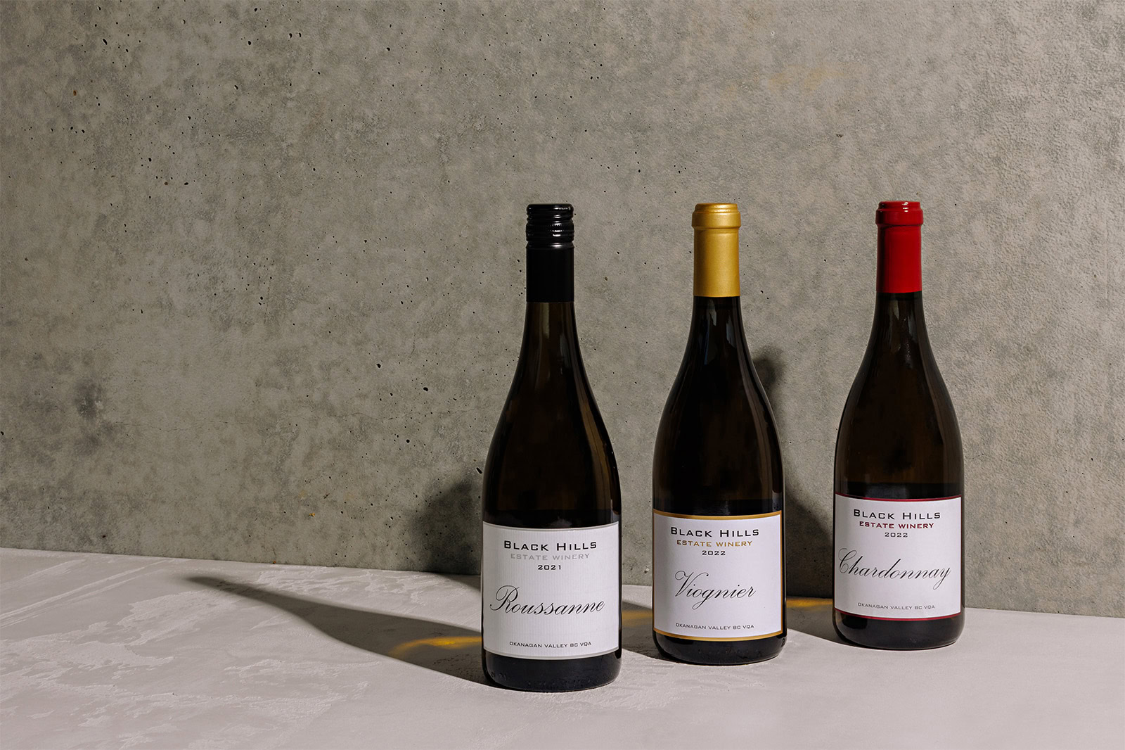 Three wine bottles are placed side by side against a concrete wall. The bottles are labeled 