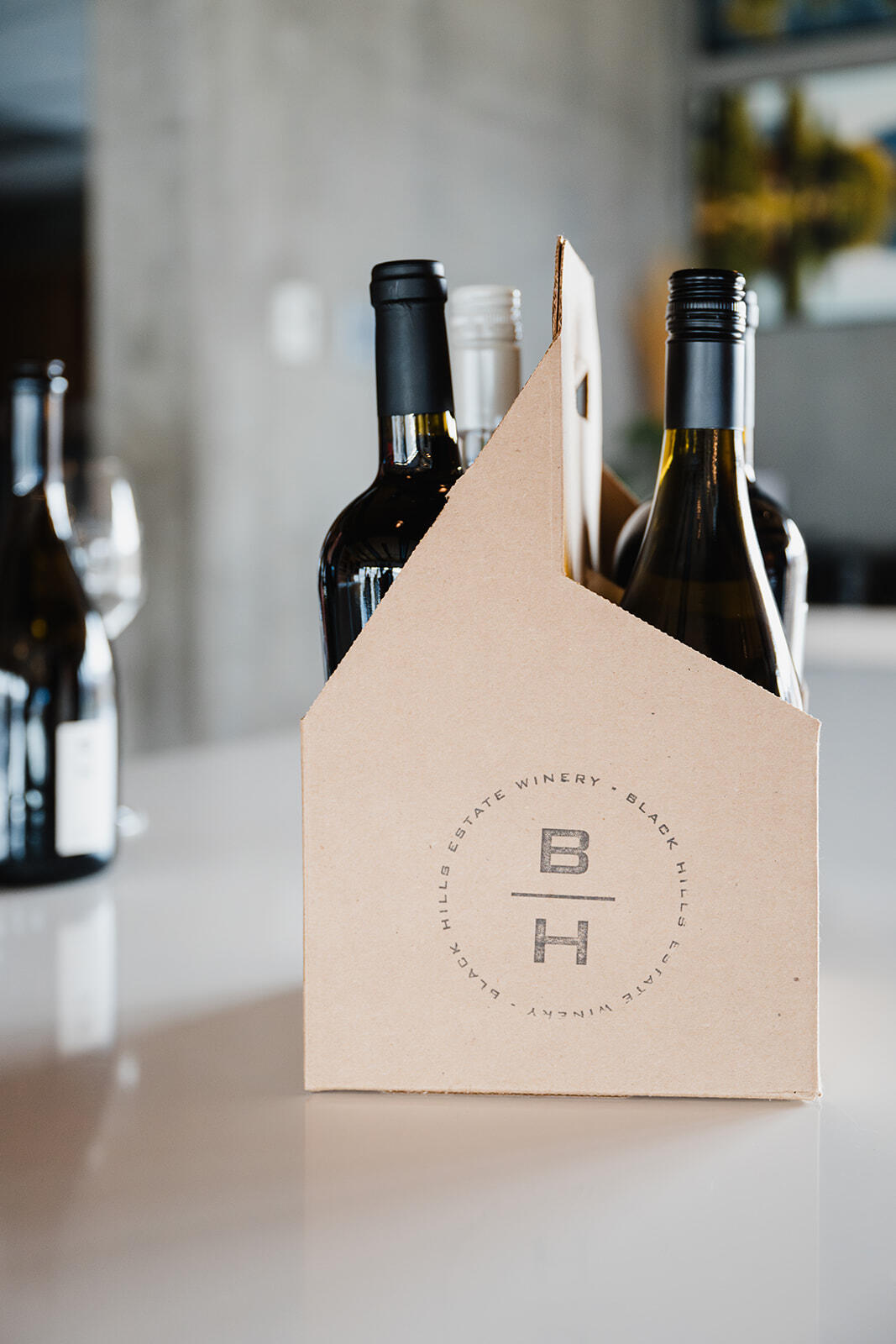 A cardboard carrier holds four various bottles of wine. The carrier displays the logo 